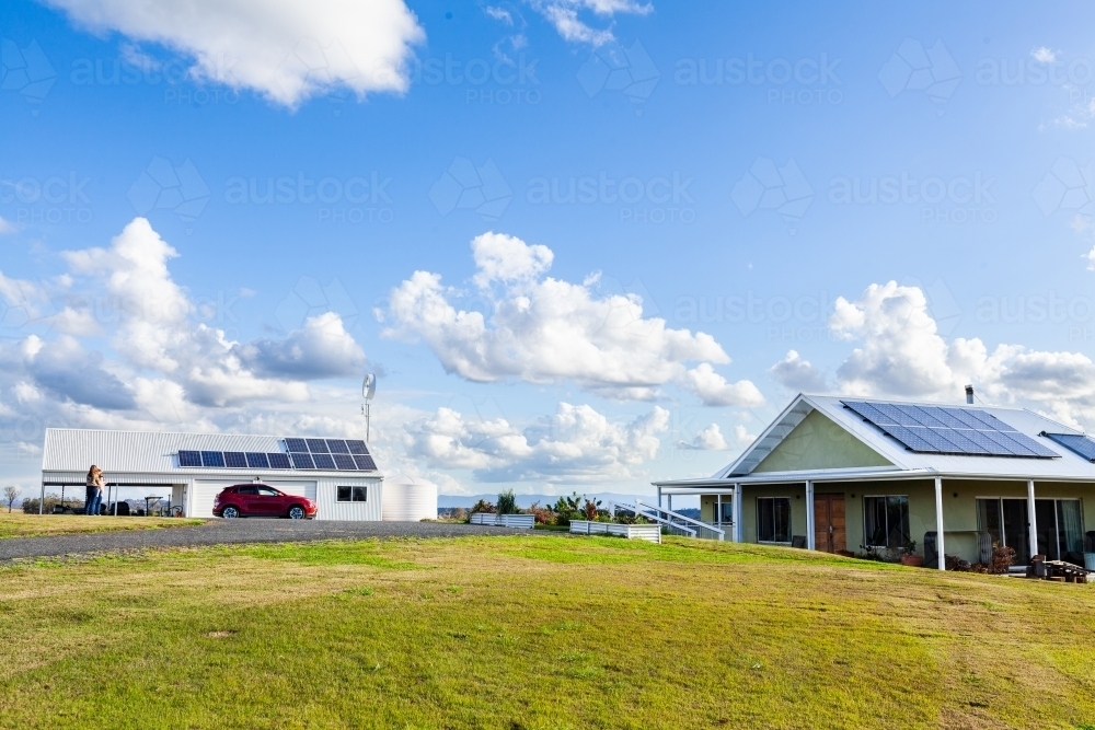 Sustainable off grid living with solar panels on house and shed roof, electric car and wind turbine - Australian Stock Image