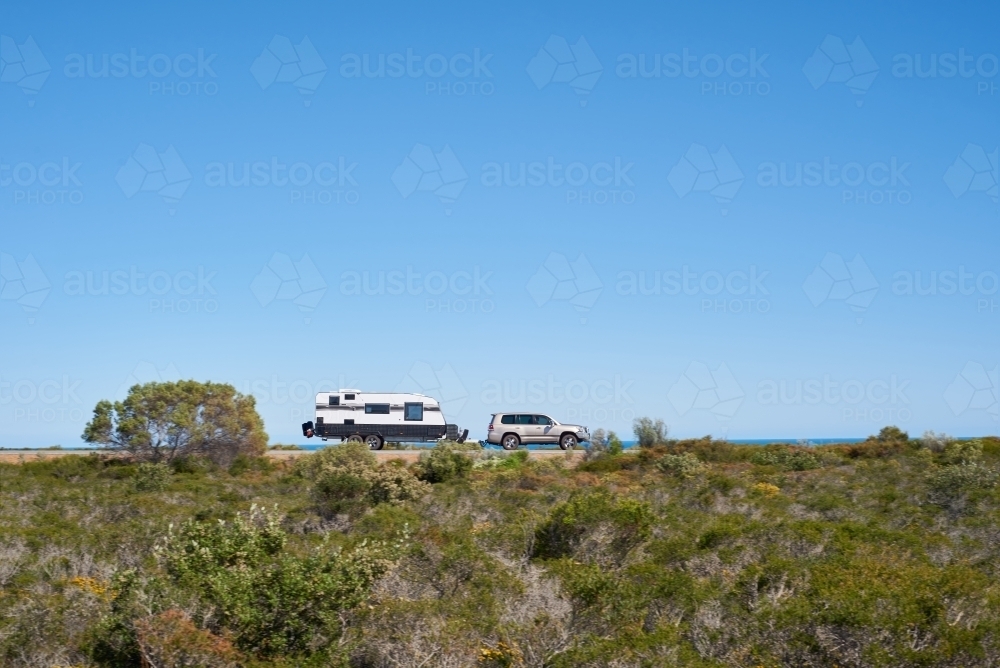 SUV towing a caravan along a coastal road in Western Australia under blue skies, with motion blur. - Australian Stock Image