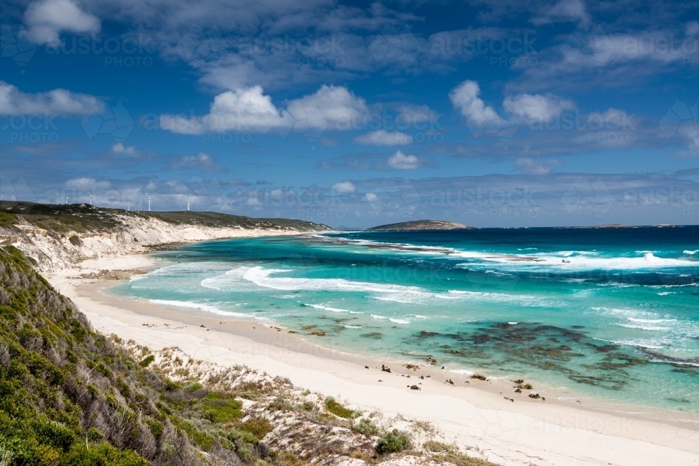 Sweeping coastal view looking down on white sandy beach with sand dunes and wind turbines - Australian Stock Image