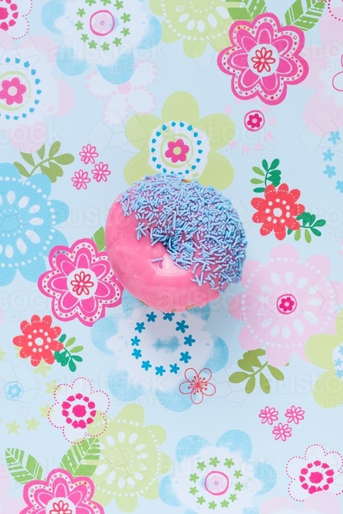 sweet donut with pink icing, blue sprinkles against a floral background - Australian Stock Image