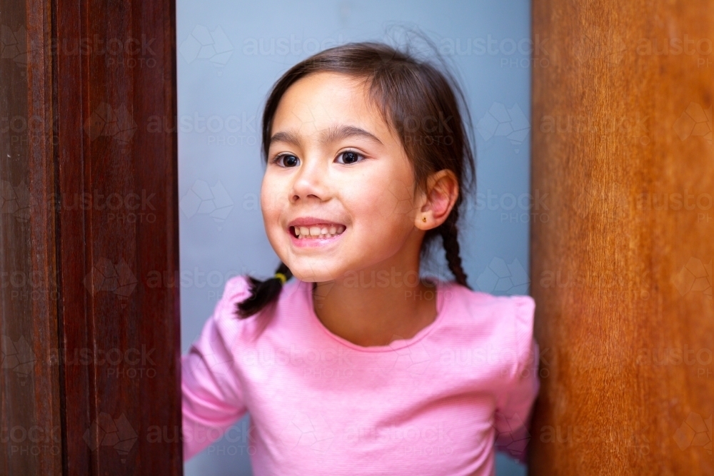 Sweet little girl looking out from half open door - Australian Stock Image