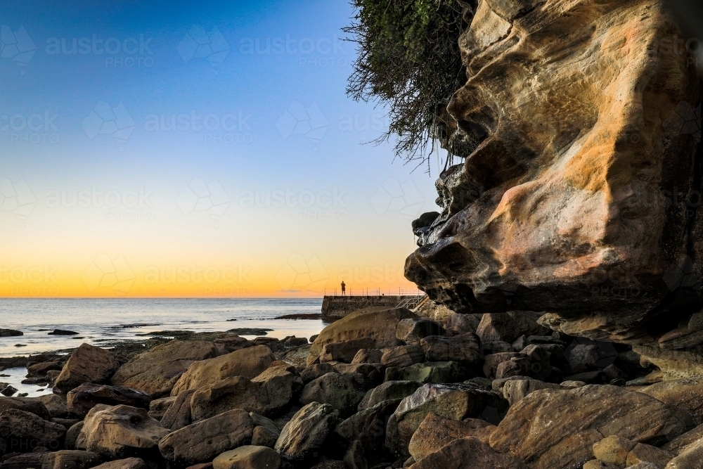 Swimmer at ocean baths against blue sky and rocky coastline - Australian Stock Image