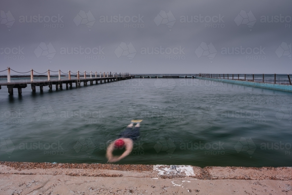 Swimmer in ocean pool on a gloomy morning - Australian Stock Image