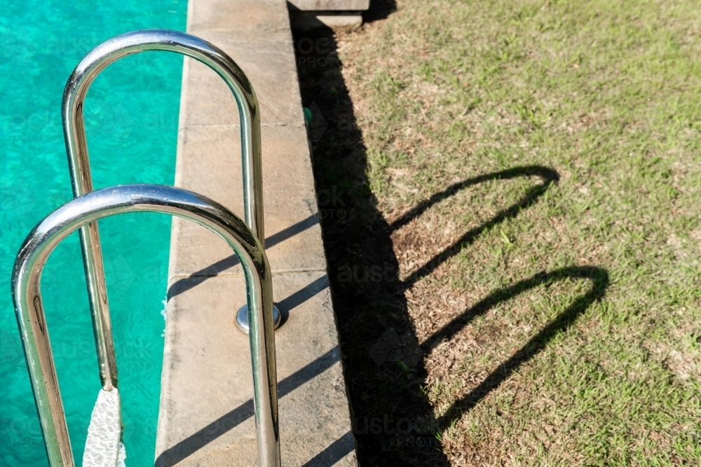 swimming pool ladder and shadow on green lawn - Australian Stock Image