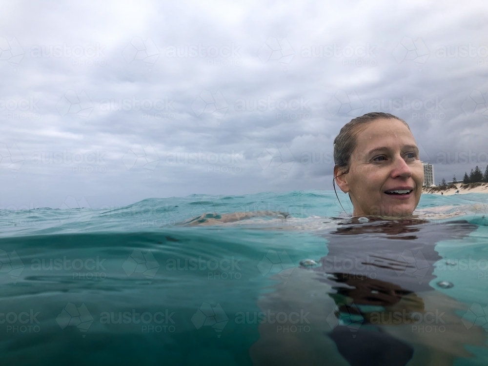 Swimming Woman with head above water in ocean looking out smiling on overcast day - Australian Stock Image