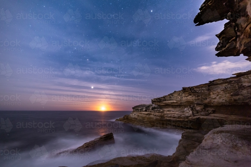 Sydney coastal cliffs by night with moonrise and light high clouds - Australian Stock Image
