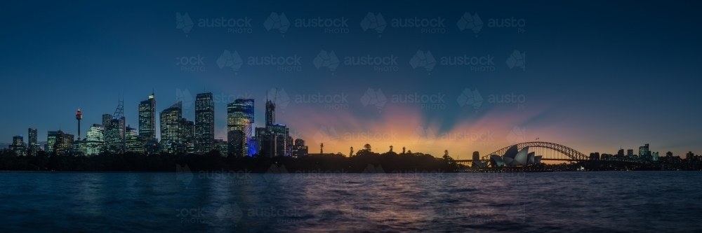 Sydney skyline and harbour after sunset with opera house and bridge in rays of dusk light - Australian Stock Image