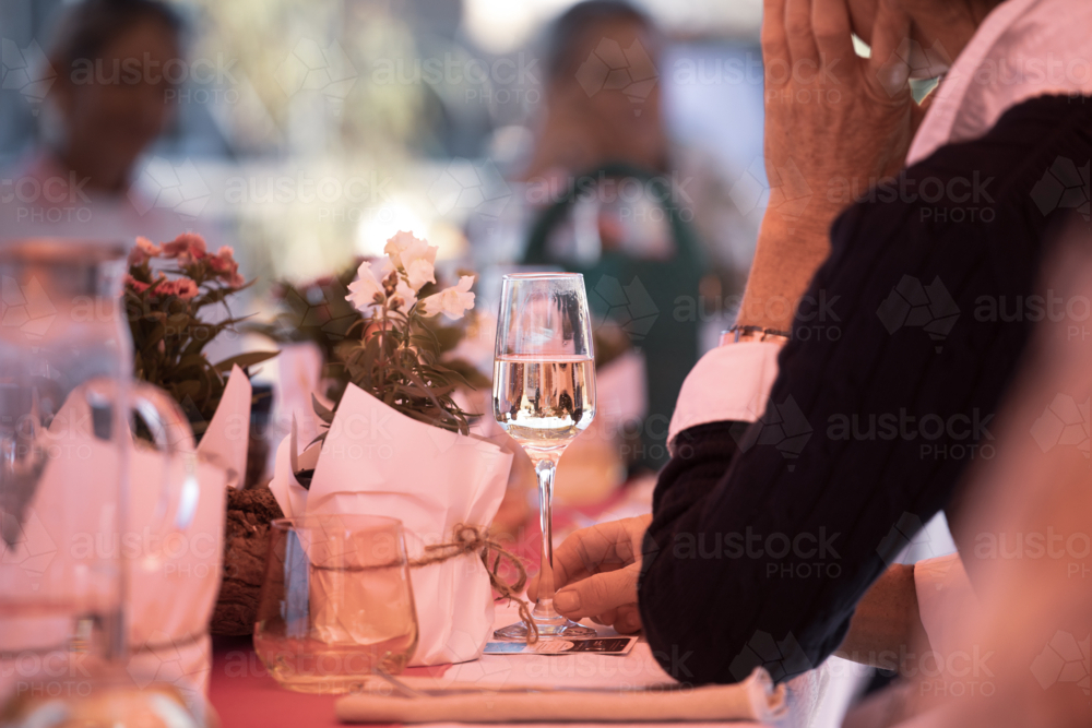 Table setting with wine glass and flowers, and people in the background - Australian Stock Image