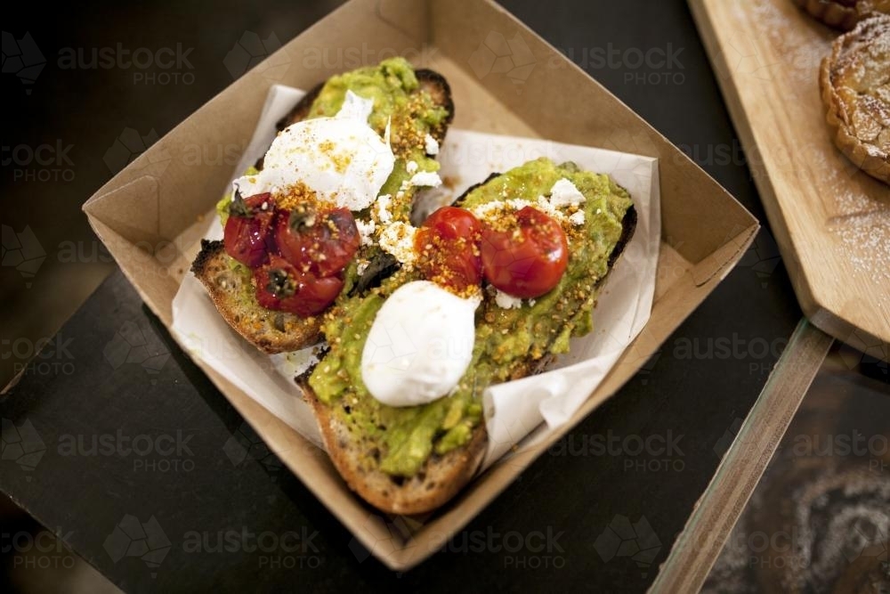 Take away toasted sandwich with avocado, poached egg and tomato - Australian Stock Image