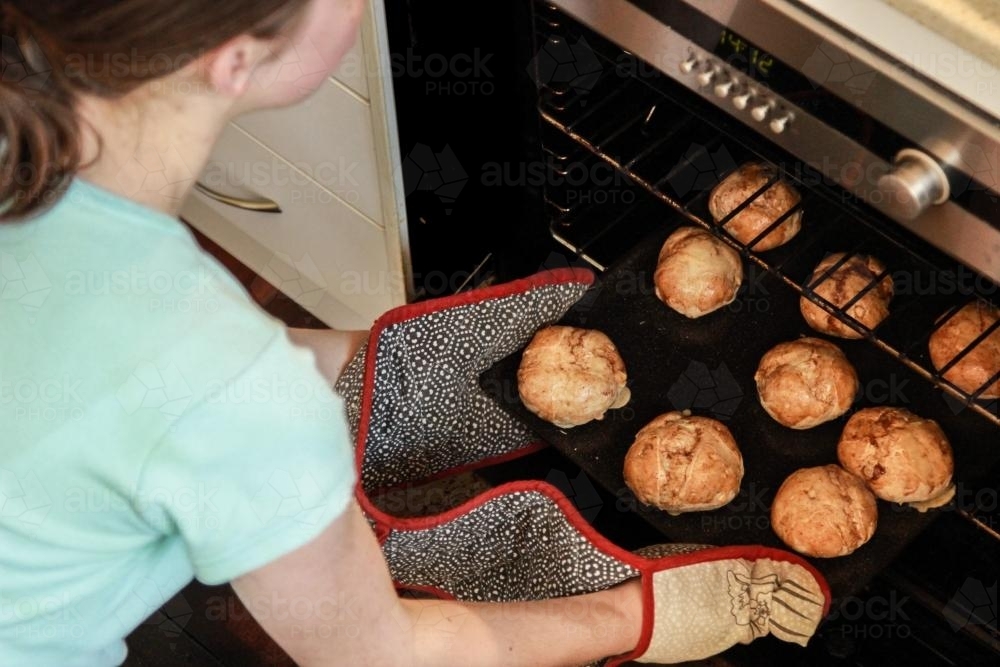 Taking hot cross buns out of the oven - Australian Stock Image