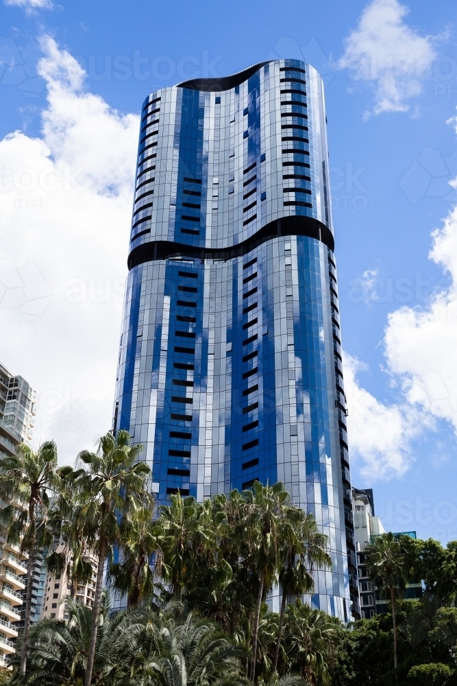 tall curved skyscraper with mirrored surface reflecting white clouds and blue sky - Australian Stock Image