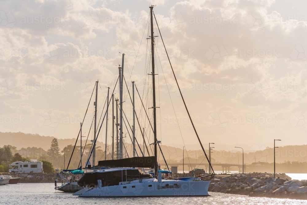 Tall masts on a row of yachts moored at a coastal marine with hazy clouds overhead - Australian Stock Image