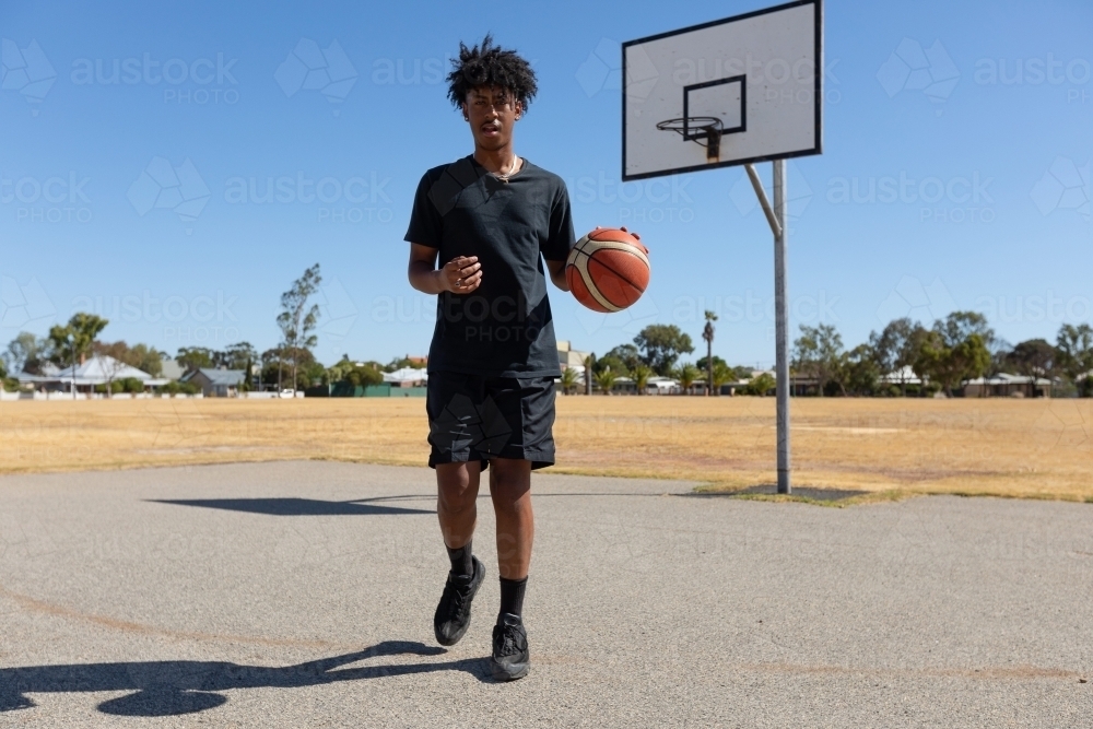 tall teenage basketball player on outdoor court with basketball - Australian Stock Image