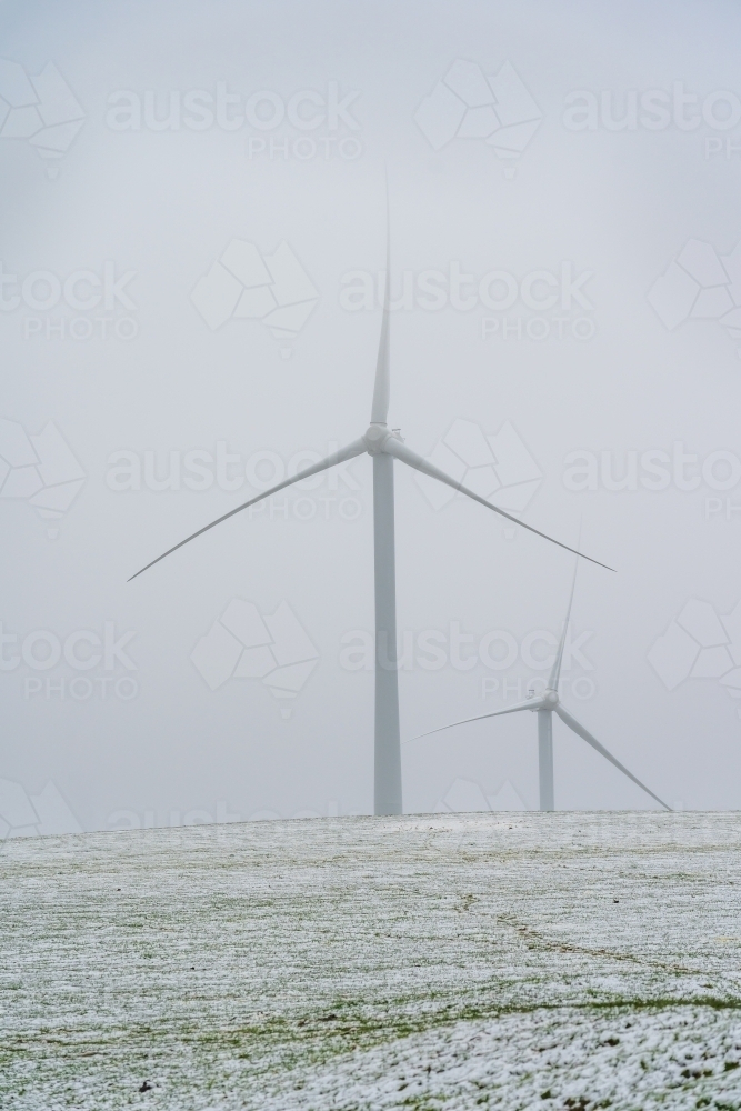 Tall wind turbines in a foggy sky on a snow covered hilltop - Australian Stock Image