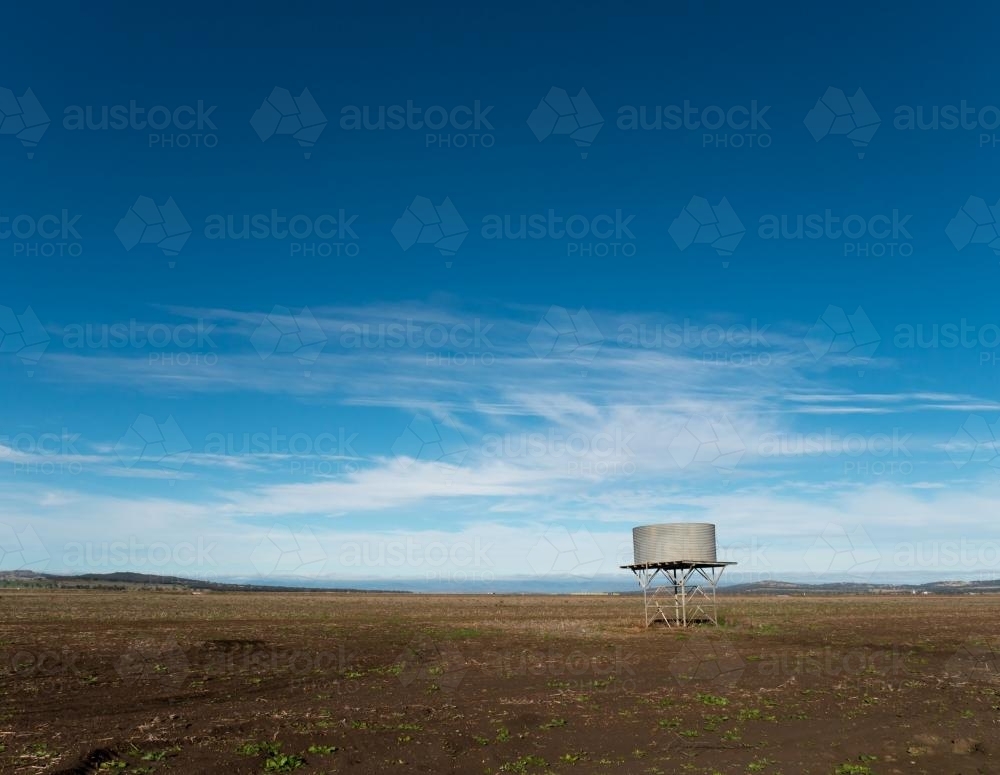 Tank stand in a treeless paddock against blue sky - Australian Stock Image