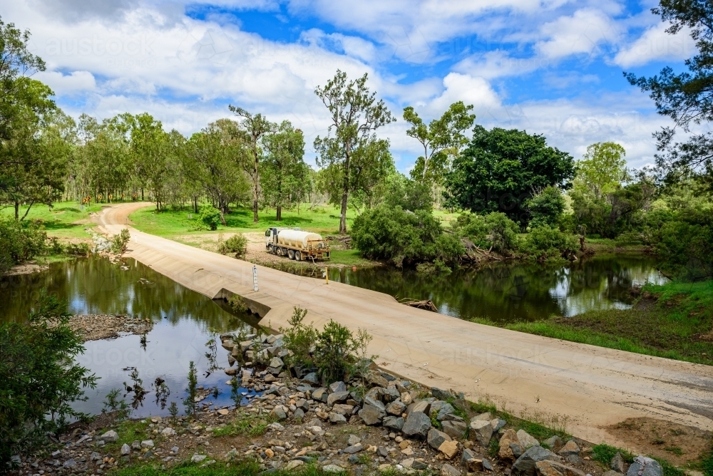Tanker truck pumping fresh water from a creek next to a concrete flood way - Australian Stock Image