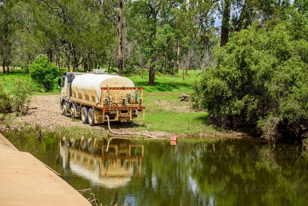 Tanker truck pumping fresh water from a creek next to a concrete flood way - Australian Stock Image