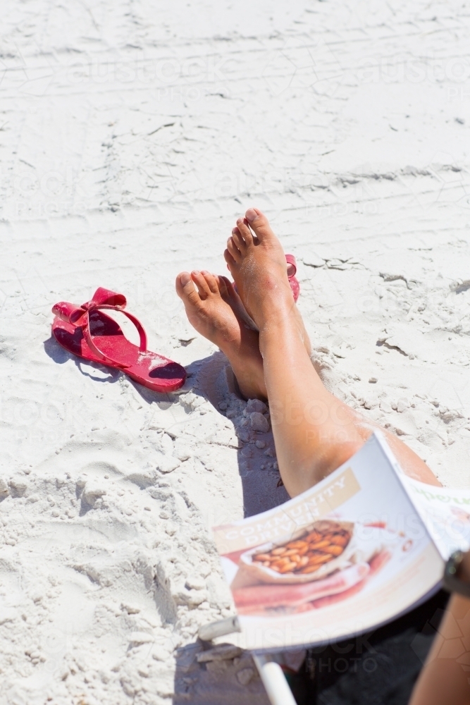 Tanned legs relaxing on a white sandy beach - Australian Stock Image