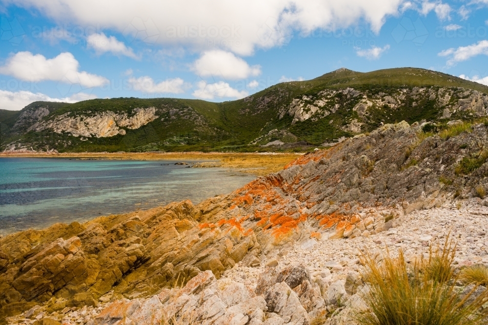 Tasmanian scenic, wild coast with orange coloured rocks and blue water - Australian Stock Image