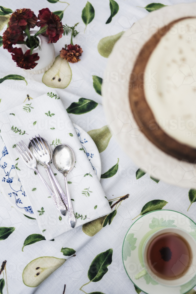Tea, cake, and cutlery resting on patterned cloth in the soft outdoor light. - Australian Stock Image