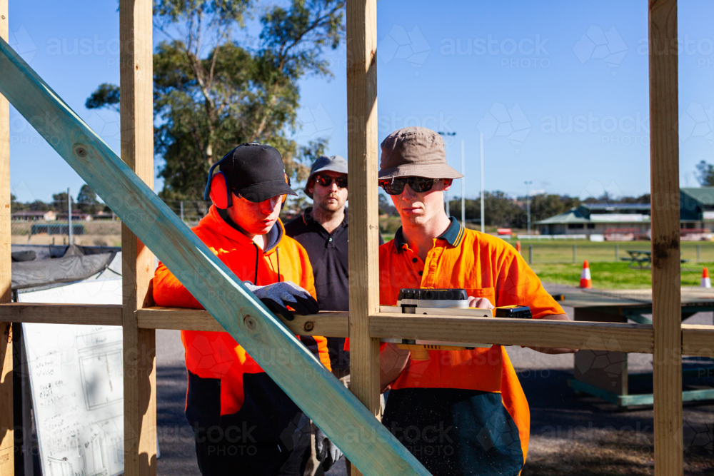 teacher instructing trade apprentices on using planer tool on building frame - Australian Stock Image
