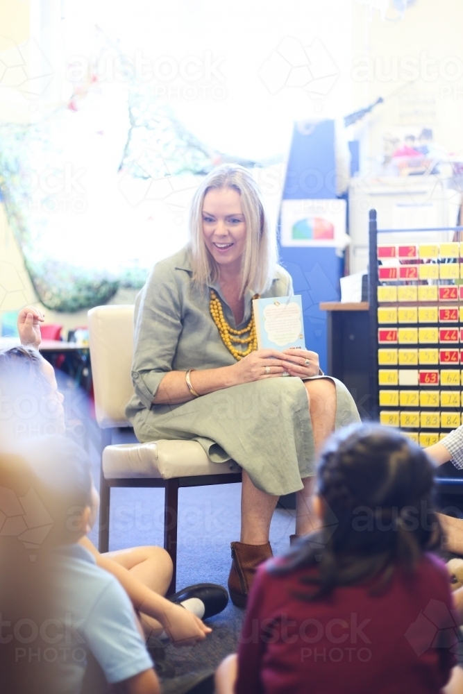 Teacher on chair, teaching children sitting on the floor - Australian Stock Image