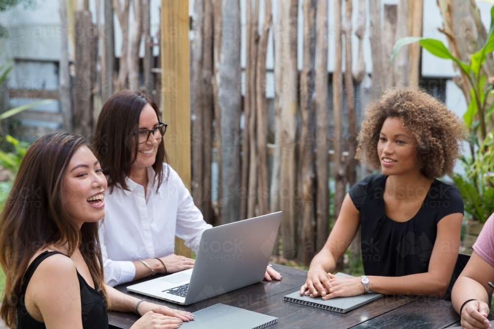 Team of women collaborating outside at a table together - Australian Stock Image
