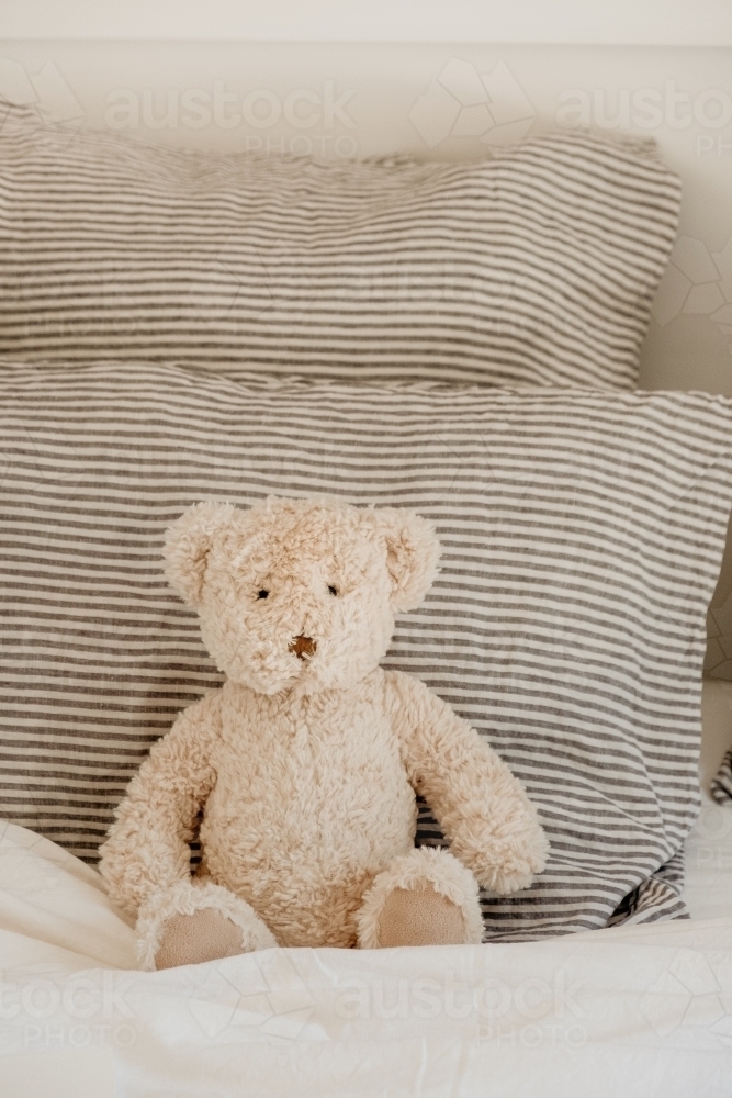 Teddy bear sits on a bed. - Australian Stock Image