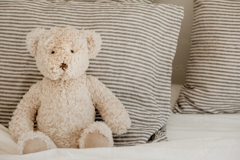 Teddy bear sits on a bed. - Australian Stock Image