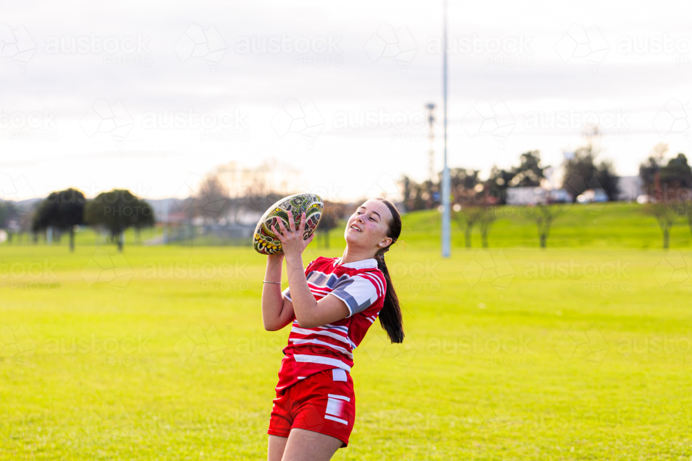 Teen aboriginal girl on sports field playing with football - Australian Stock Image