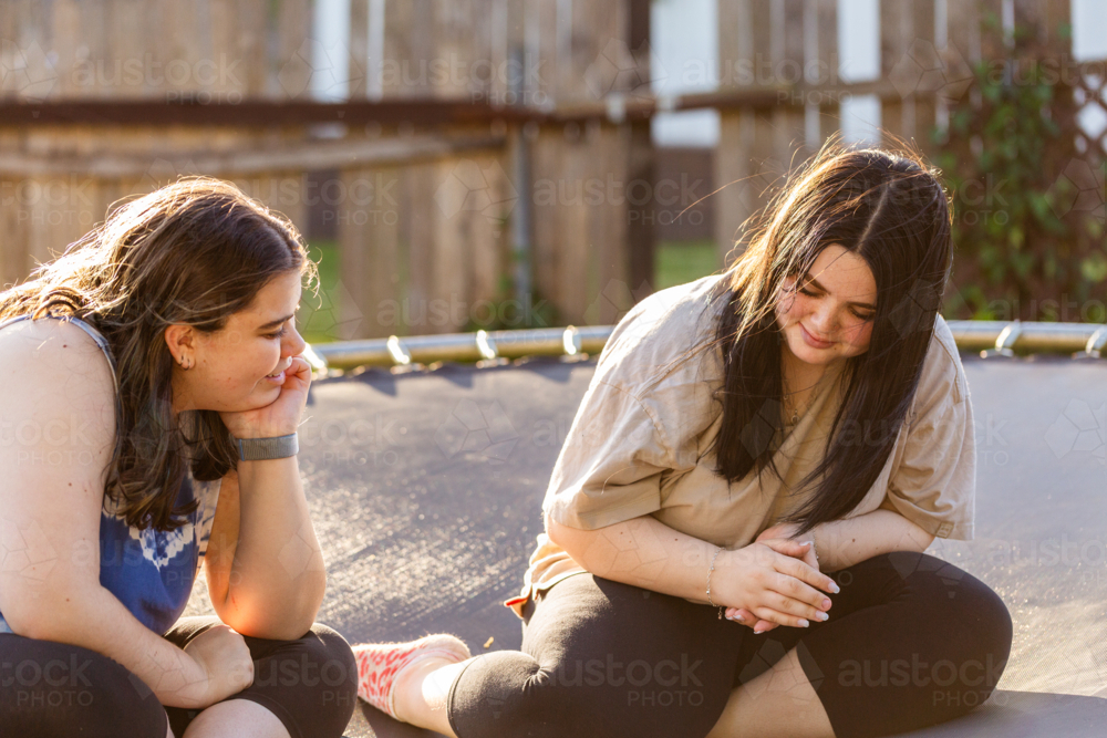 Teen aboriginal sisters sitting together on trampoline in backyard - Australian Stock Image
