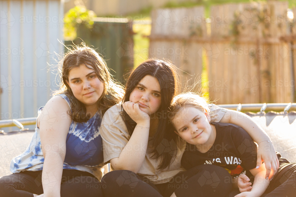 Teen aboriginal sisters sitting together on trampoline in backyard - Australian Stock Image