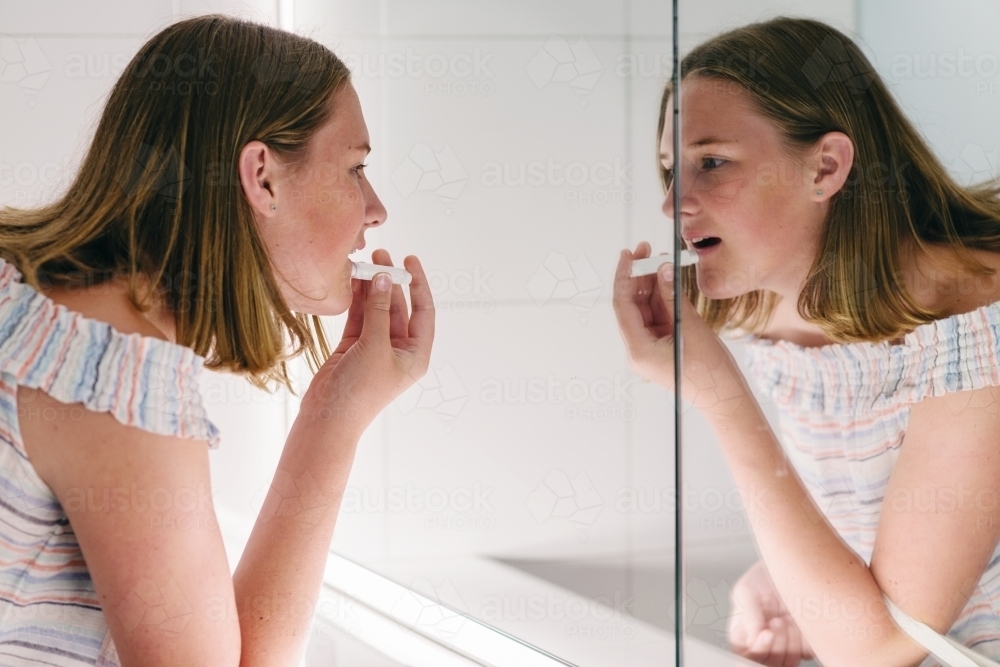 teen applying lip balm in bathroom mirror - Australian Stock Image