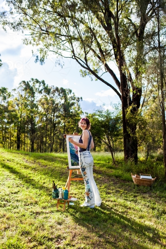 Teen artist standing beside painting in australian bushland clearing - Australian Stock Image