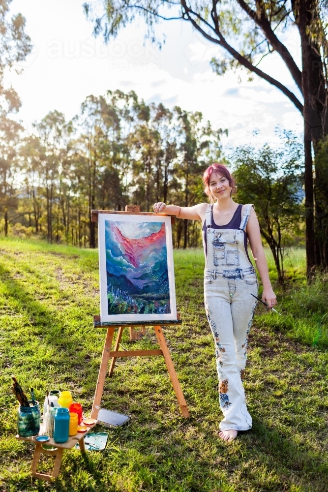 Teen artist standing beside painting in australian bushland clearing - Australian Stock Image