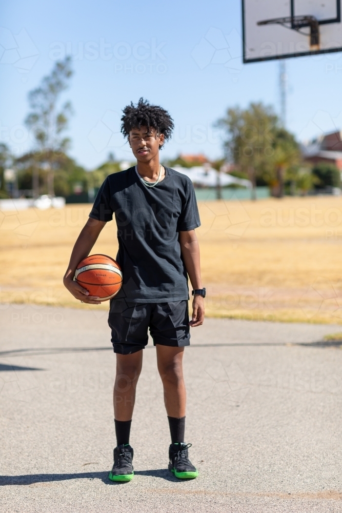 teen basketballer standing on outdoor court holding ball - Australian Stock Image