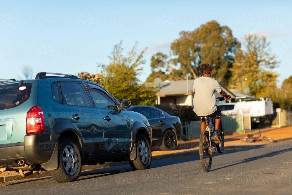 teen boy doing wheelie on bicycle on quiet street - Australian Stock Image