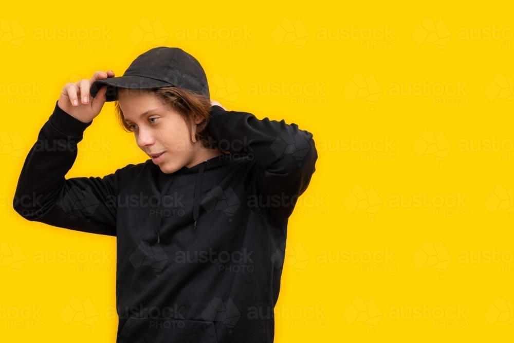 teen boy dressed in black with cap on yellow background - Australian Stock Image