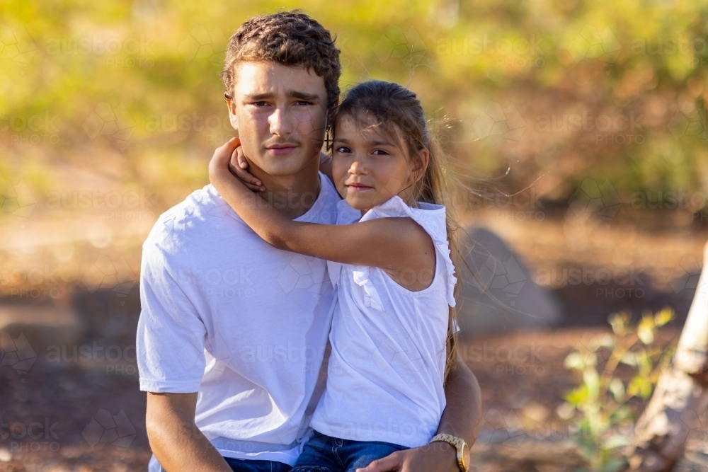 Teen boy holding his little sister outdoors - Australian Stock Image