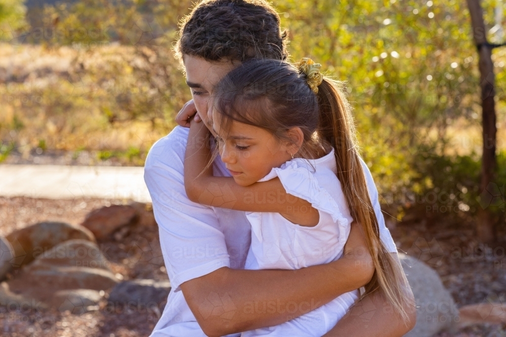 teen boy holding his younger sister with arms around each other - Australian Stock Image