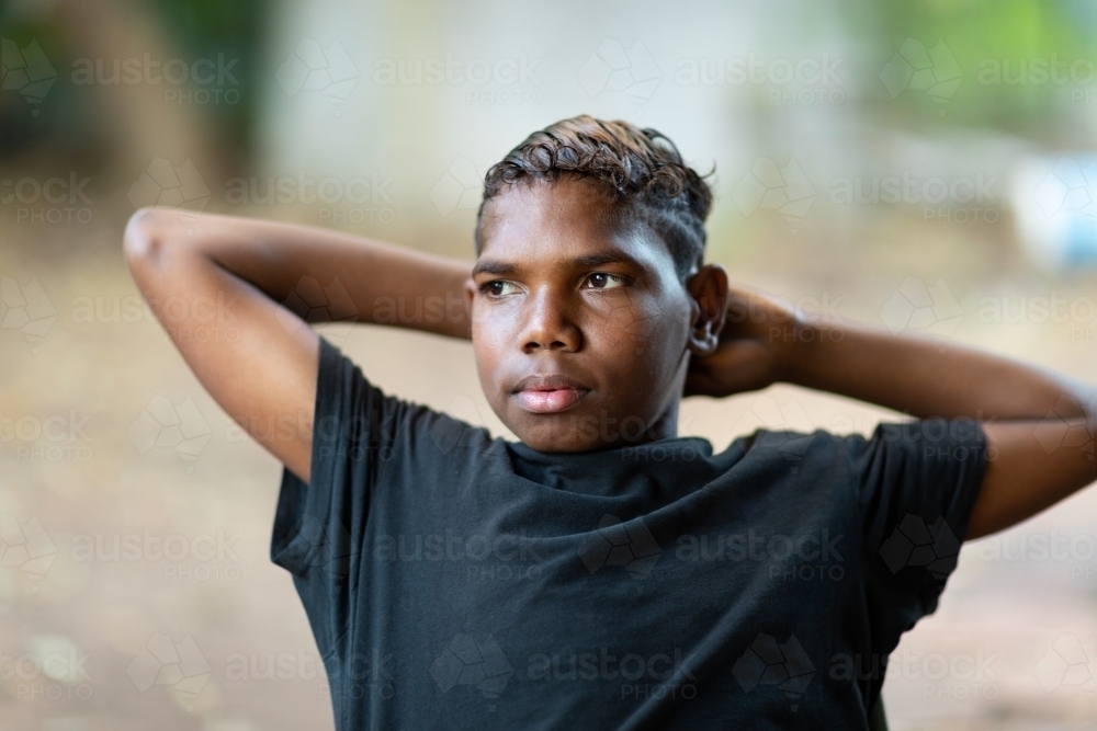 teen boy in black leaning back with arms behind his head - Australian Stock Image
