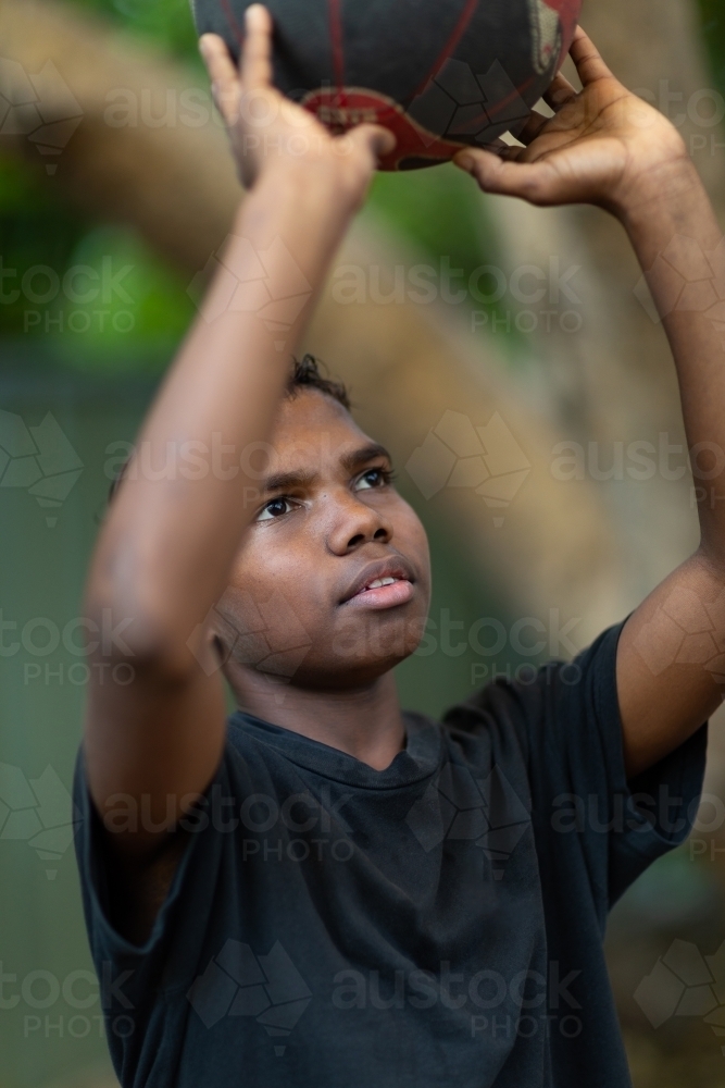 teen boy in black looking up to aim basketball shot - Australian Stock Image