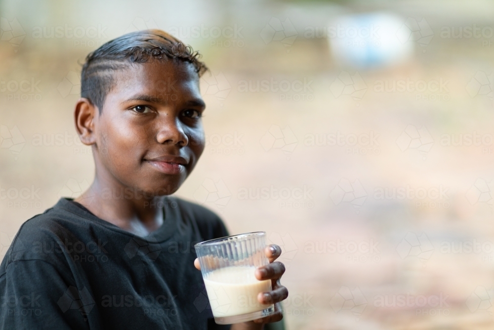 teen boy in black tee holding milk drink in glass looking at camera - Australian Stock Image