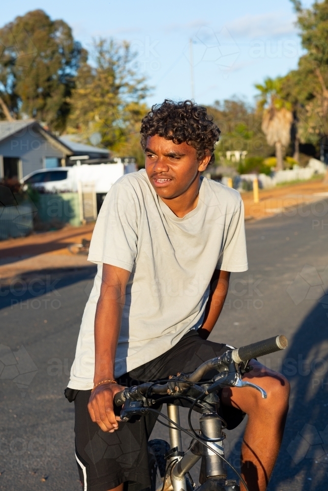 teen boy resting on bike in street - Australian Stock Image