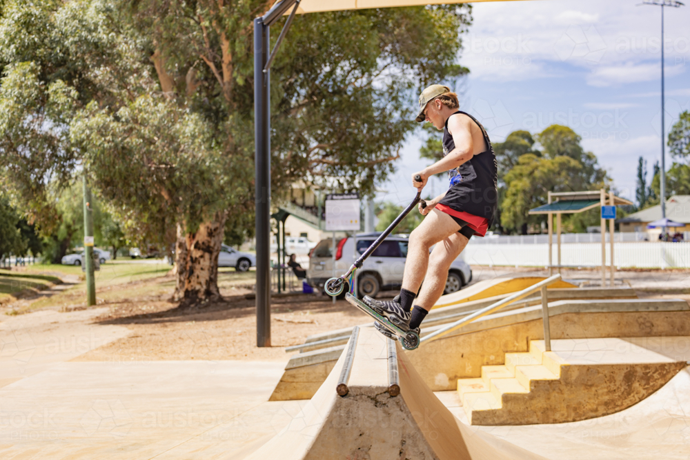 Image of Teen boy riding scooter on ramps at skate park - Austockphoto