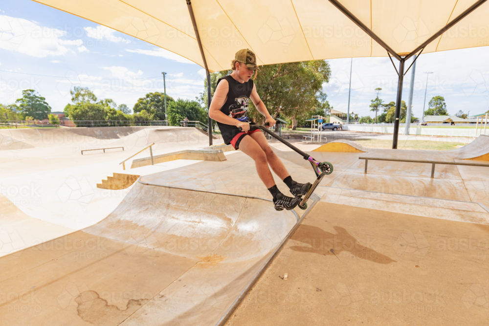 Image of Teen boy riding scooter on ramps at skate park - Austockphoto