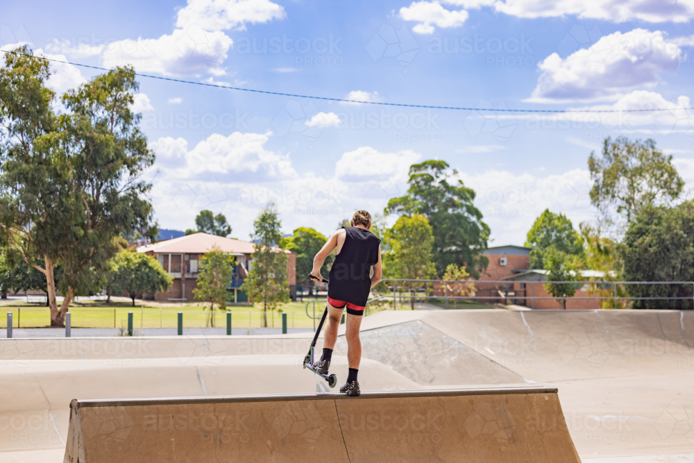 Image of Teen boy riding scooter on ramps at skate park - Austockphoto