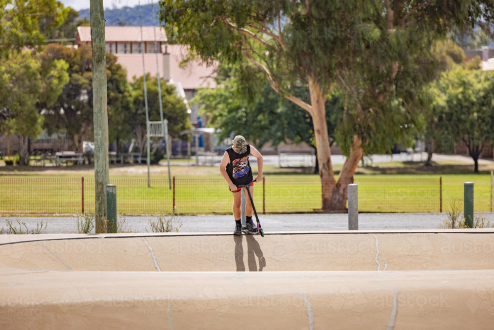 Image of Teen boy riding scooter on ramps at skate park - Austockphoto