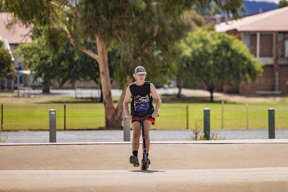 Image of Teen boy riding scooter on ramps at skate park - Austockphoto
