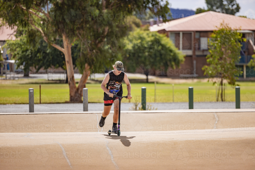 Image of Teen boy riding scooter on ramps at skate park - Austockphoto